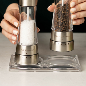 A person with manicured nails holds a Cole & Mason Derwent Mill Christmas Gift Hamper, featuring stainless steel mills filled with coarse salt and black peppercorns—an elegant addition to any festive gift collection.