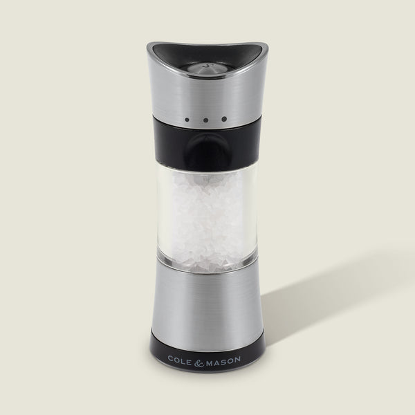 A Cole & Mason Horsham Salt & Pepper Mill in stainless steel and clear acrylic, filled with coarse salt, stands upright on a light background with a right-side shadow and the COLE & MASON logo at its base.