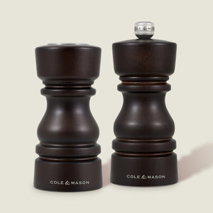 The Cole & Mason London Chocolate Wood Salt Shaker & Pepper Mill Set features two dark wood mills: the pepper mill with grind select technology and a knob, and the shorter, knob-less salt shaker with a premium grinding mechanism.