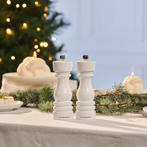 A Cole & Mason London White Gloss Mill Christmas Gift Hamper adds elegance to a festive table with a white cloth, pine branches, candles, and a twinkling tree—perfect for any Christmas gift box.