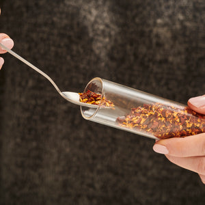 A person scoops red pepper flakes from a Cole & Mason Shadwell Countertop Spice Storage, demonstrating practical and stylish spice organization.