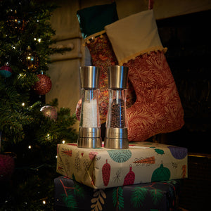 The Cole & Mason Derwent Mill Christmas Gift Hamper sits among wrapped presents beneath a decorated tree and stockings, with warm festive lighting setting a cozy holiday mood—an ideal Christmas gift.