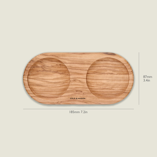 The Cole & Mason Portobello Olive Wood Mill Tray features an oval shape with two circular indentations, ideal for holding salt and pepper mills. It measures 185mm x 87mm and is shown against a plain background.