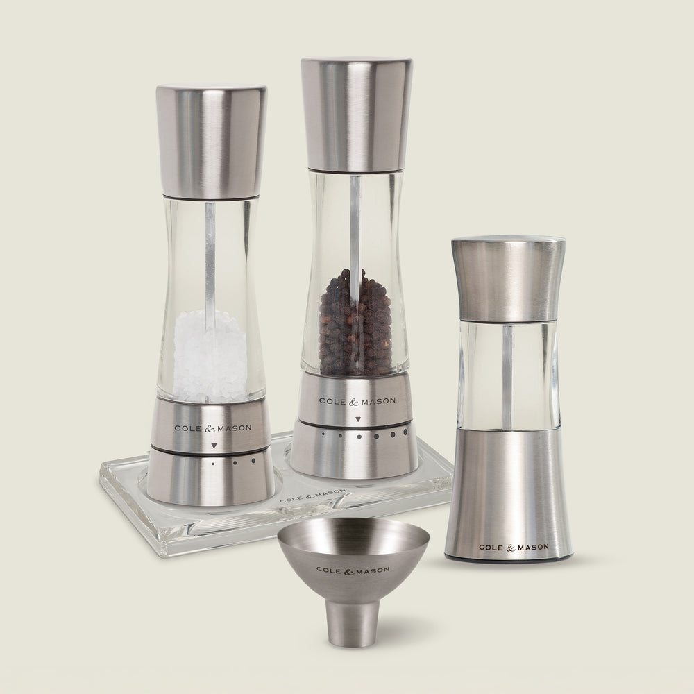 The Cole & Mason Derwent Mill and Stadhampton Chilli Mill Seasoning Set includes matching mills with a funnel and tray, filled with salt, peppercorns, and chili. Both grinders are displayed on a neutral background.