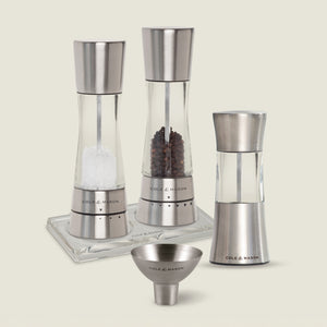 The Cole & Mason Derwent Mill and Stadhampton Chilli Mill Seasoning Set includes matching mills with a funnel and tray, filled with salt, peppercorns, and chili. Both grinders are displayed on a neutral background.