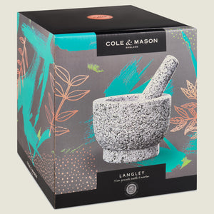 The Cole & Mason Langley Pestle & Mortar box features a photo of the natural granite set with teal and orange leaf designs on a gray background—ideal for preparing fresh spice rubs.
