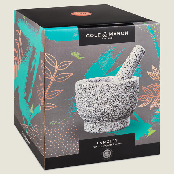 The Cole & Mason Langley Pestle & Mortar box features a photo of the natural granite set with teal and orange leaf designs on a gray background—ideal for preparing fresh spice rubs.