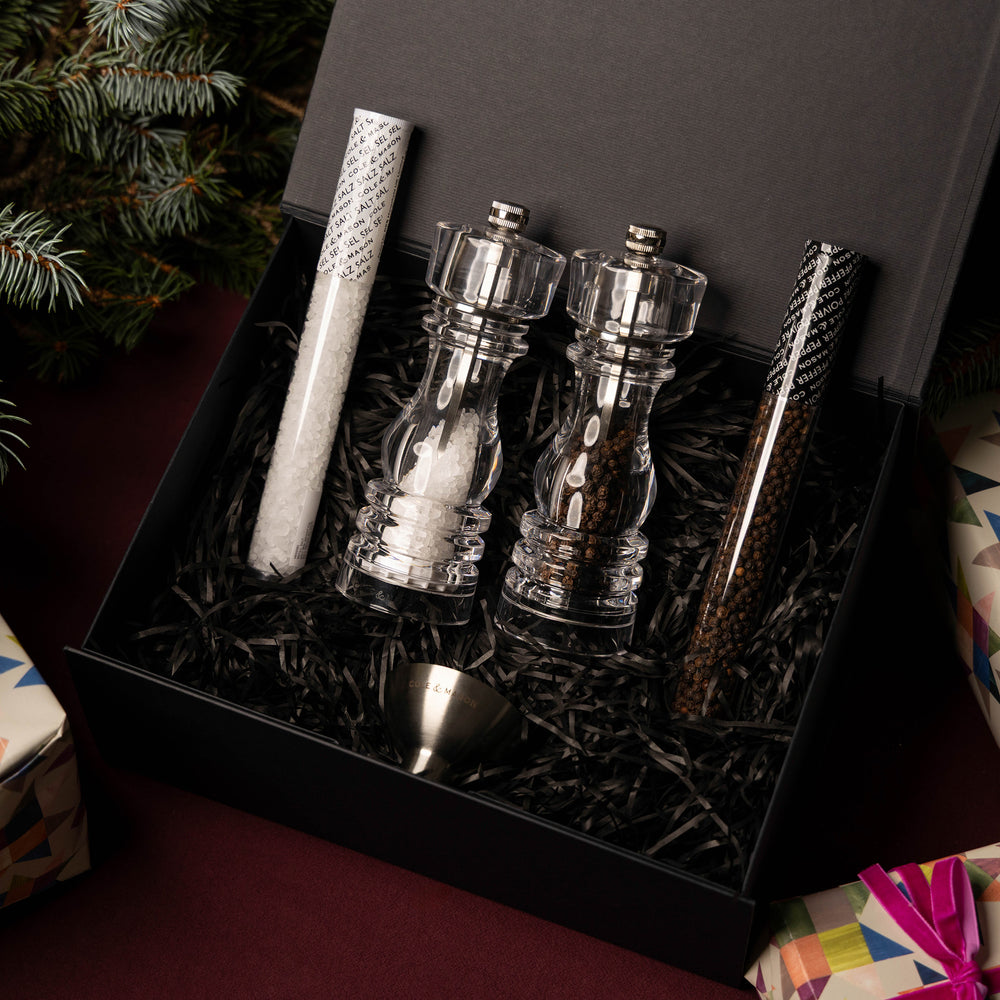 The London Acrylic Mill Christmas Gift Hamper by Cole & Mason includes a sleek black box with shredded paper, featuring a salt and pepper mill set, two spice tubes, and a metal funnel all neatly arranged inside.