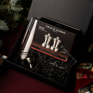 The Hoxton Silver Plated Mill Christmas Gift Hamper by Cole & Mason includes a salt and pepper mill set, metal funnel, two glass tubes with salt and pepper, and an acrylic stand on black shred—ideal for festive Christmas hampers.