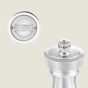 Close-up view of a metallic Cole & Mason pepper or salt grinder, showing the top knob labeled S and an inset image displaying the grinders base with engraved branding and text Since 1919.