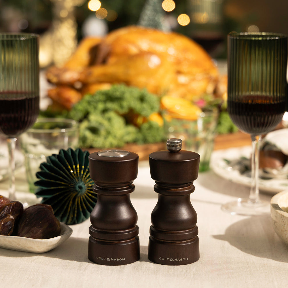 A black gift box with shredded paper holds the Cole & Mason London Chocolate Wood Mill & Shaker Christmas Gift Hamper, featuring wooden mills and shaker, a stainless steel funnel, all neatly arranged inside with the lid open.