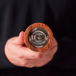 #salt&pepperset A person holds a Cole & Mason Portobello Olive Wood Salt & Pepper Mill toward the camera, highlighting its precision grinding mechanism and branded base.