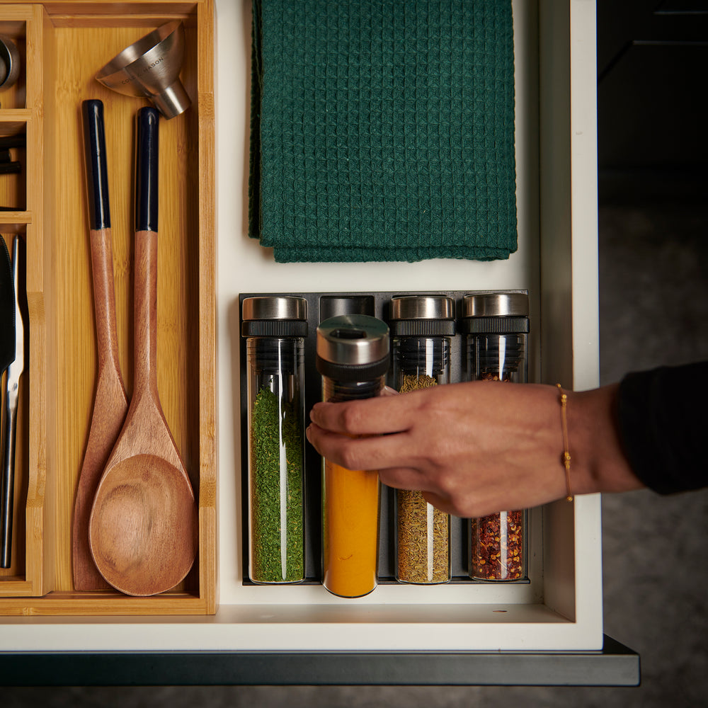 A set of four clear, airtight glass jars with black lids, laid horizontally in a sleek black rack labeled Cole & Mason—a stylish Shadwell Drawer-Fit Spice Storage set for your kitchen.