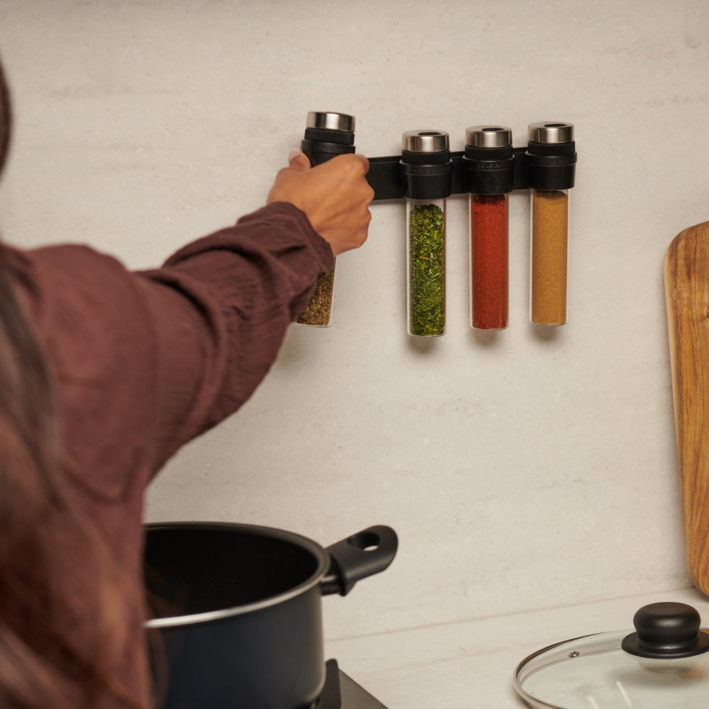 The Cole & Mason Shadwell Slim-Mount Spice Storage features four clear airtight glass containers with silver lids in a vertical black wall rack—ideal for stylish herb and spice storage.
