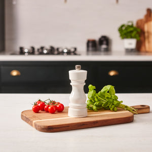 #salt The Cole & Mason London White Acrylic Salt & Pepper Mill (150mm) is arranged on a wooden cutting board with fresh basil and cherry tomatoes in a modern kitchen with a blurred background.