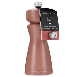 A Cole & Mason Kenton Salt & Pepper Mill in Cinnamon features a rose-colored body with a silver top, labeled for use with either salt or pepper. Showcasing a modern design and equipped with a durable ceramic grinder, the mill includes a tag near the top displaying the Cole & Mason branding and usage instructions.