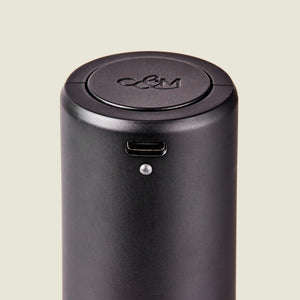 Close-up of the Cole & Mason Brixton Electric Mill Matt Black GS, a cylindrical black electronic device featuring a USB-C port and a small indicator light. Designed for one-handed operation, this electric mill has an embossed C&M logo on its circular lid and contains a durable ceramic grinder inside.