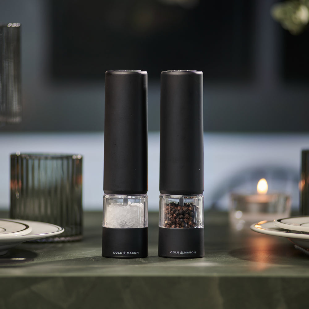 Two sleek, matt black electric grinders labeled Cole & Mason Brixton Electric Mill stand side by side against a plain, light background, each featuring a durable ceramic grinder for smooth and precise seasoning with convenient one-hand operation.