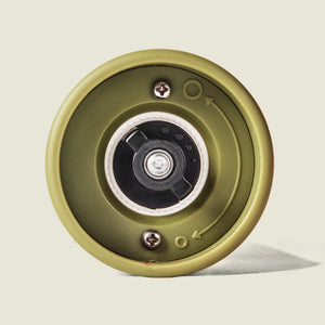 Close-up of the bottom of the Cole & Mason Brixton Electric Mill Olive Green GS, highlighting its green cylindrical design, visible screws, a rotating mechanism with a ceramic grinder, and directional arrows for convenient one-handed operation.