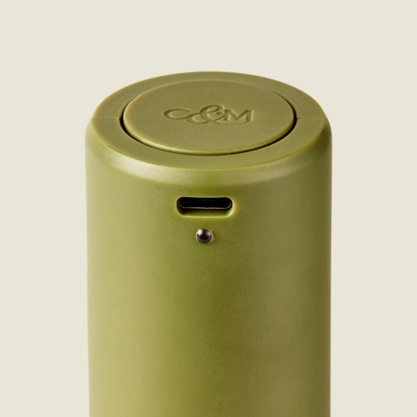 A close-up of the Brixton Electric Mill Olive Green GS by Cole & Mason, a sleek green cylindrical electric salt and pepper mill with a small hole and button or sensor for easy one-handed operation, featuring Cole & Mason branding engraved on the top, set against a simple light background.