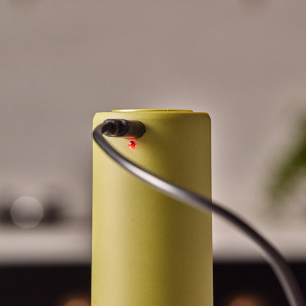 A close-up of the Cole & Mason Brixton Electric Mill Olive Green GS, a cylindrical electronic device designed for one-handed use, with a black cable plugged in and a small red indicator light turned on. The electric salt and pepper mill features a durable ceramic grinder for efficient seasoning.