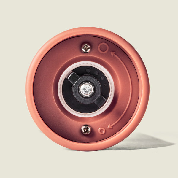 Close-up of the bottom of a Cole & Mason Brixton Electric Mill Terracotta GS, highlighting a central metal screw, two smaller screws, an adjustment dial, and directional arrows—a design echoing the precision ceramic grinding system found in this high-end electric mill.