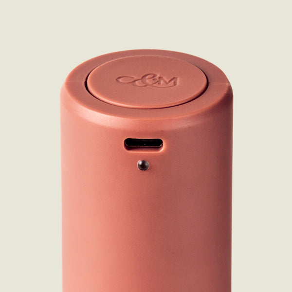 A close-up of the Cole & Mason Brixton Electric Mill Terracotta GS, a cylindrical, reddish-brown rechargeable mill with a small USB-C port and indicator light on its side, featuring an embossed logo on the top.