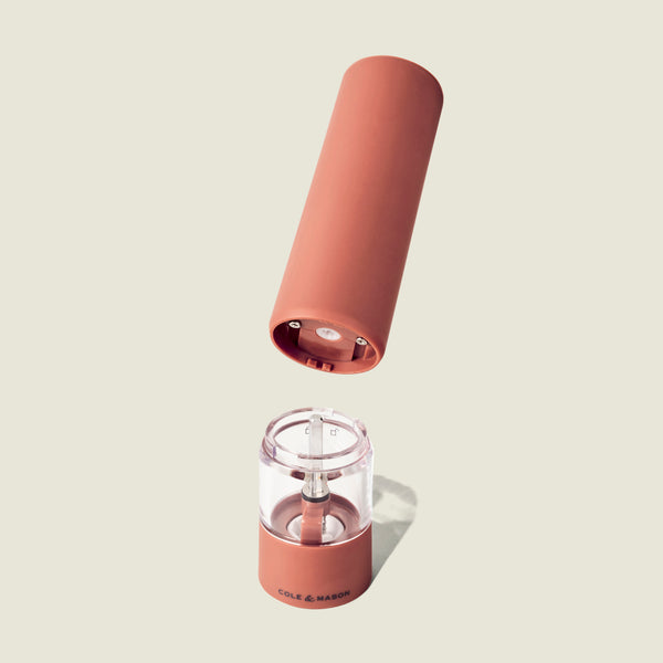 The Cole & Mason Brixton Electric Mill Terracotta GS is a rechargeable grinder in a warm terracotta hue, featuring a ceramic grinding mechanism. Its top section appears to float above the transparent lower body, showcasing the internal components. The Cole & Mason brand is displayed on the base, and modern convenience is provided by USB-C charging.