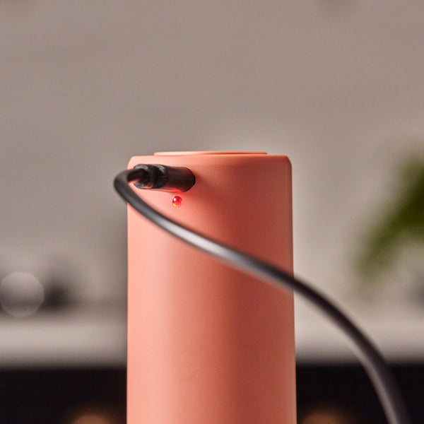 A close-up of the Cole & Mason Brixton Electric Mill Terracotta GS being charged, with a black USB-C charging cable connected and a small red indicator light illuminated.