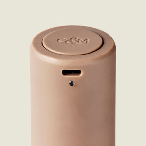 The Brixton Electric Mill Stone GS by Cole & Mason is a beige, cylindrical grinder with the C&M logo on top, featuring a small rectangular port and a subtle button or indicator beneath it. Designed with an adjustable grind and a robust ceramic grinding core, this mill stands out against the light, plain background.