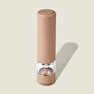 A tan, cylindrical Cole & Mason Brixton Electric Mill Stone GS pepper grinder with a transparent mid-section displaying peppercorns inside, featuring adjustable grind settings for customized seasoning, stands upright on a light background with the brand name visible at its base.