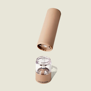 A tan, battery-operated Cole & Mason Brixton Electric Mill Stone GS is shown with its top section removed to reveal the ceramic grinding core and battery compartment below, set against a plain light beige background.