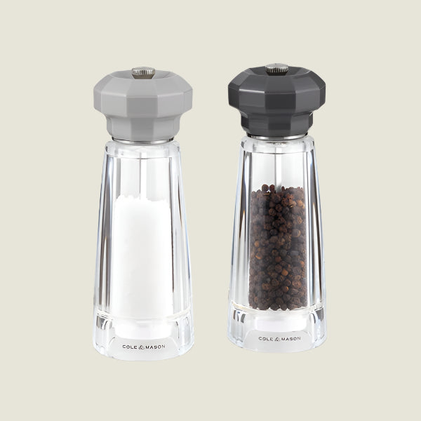 The Cole & Mason Lowestoft Salt & Pepper Mill Set 175mm includes two clear acrylic grinders with gray tops, adjustable ceramic mechanisms, and branding at the base—one filled with white salt, the other with black peppercorns.