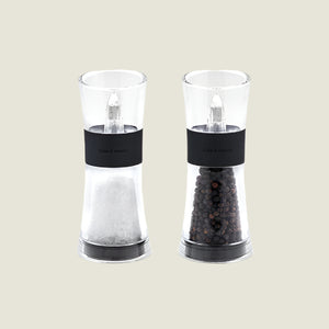 The Cole & Mason UK Flip Inverta Salt & Pepper Mill Set Black 155mm features two clear mills with black bands, one for coarse salt and one for whole black peppercorns, each with a quality grinding mechanism, shown on a light background.