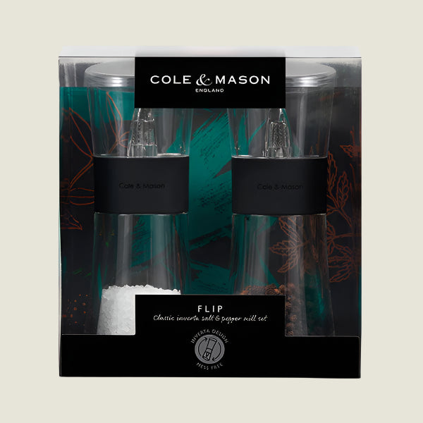 The Cole & Mason UK Flip Inverta Salt & Pepper Mill Set Black 155mm features a durable grinding mechanism, clear mills with black bands showing visible salt and pepper, and comes in decorative teal and brown leaf-patterned packaging.