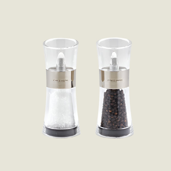 The Cole & Mason Flip Salt & Pepper Mill Set features two transparent mills with silver bands, one filled with Belgian sea salt and the other with Vietnamese peppercorns, displayed side by side on a light background.