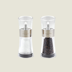 The Cole & Mason Flip Salt & Pepper Mill Set features two transparent mills with silver bands, one filled with Belgian sea salt and the other with Vietnamese peppercorns, displayed side by side on a light background.