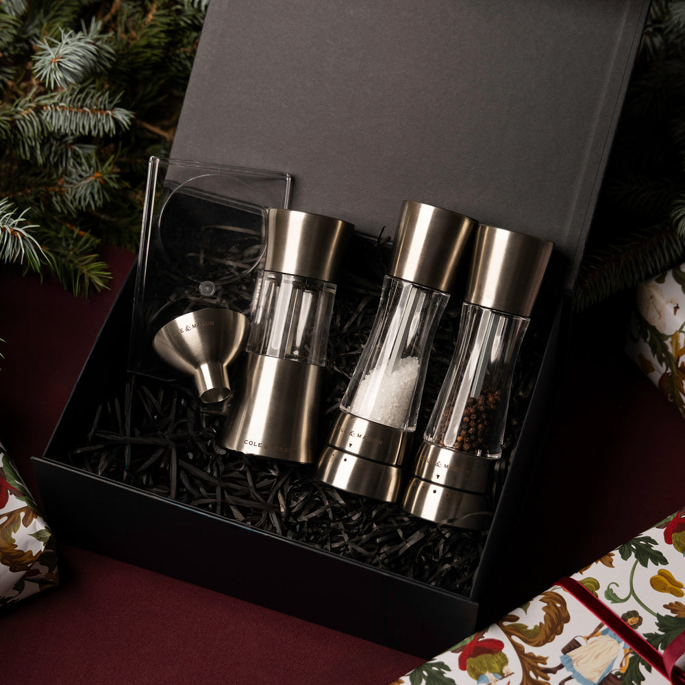 The Derwent Mill Christmas Gift Hamper by Cole & Mason features salt and pepper mills, a metal funnel, and a branded box with spice grinder image—all presented in black shredded paper. Perfect as a festive gift hamper.