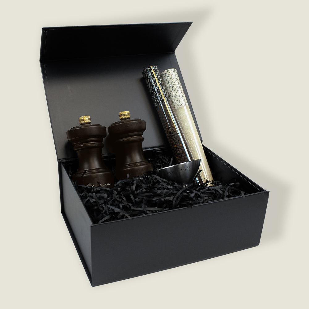 The Hoxton Chocolate Wood Mill Christmas Gift Hamper by Cole & Mason features two dark wooden mills, two spice refills in clear tubes, and a metal scoop, all presented in a black gift box—a perfect choice for gifting.