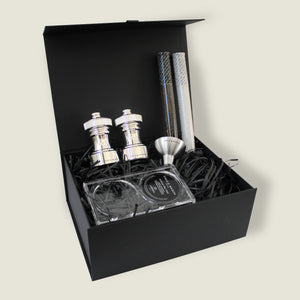 The Cole & Mason Hoxton Silver Plated Mill Christmas Gift Hamper features two silver spice grinders, two containers, a metal funnel, labels, and a clear tray in a black gift box with shred—open to display all items neatly for gifting.