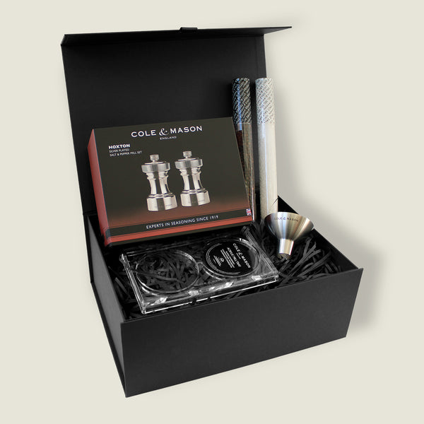 The Cole & Mason Hoxton Silver Plated Mill Christmas Gift Hamper includes salt and pepper mills, two mesh tubes, a silver funnel, and a clear tray in a sleek black box—perfect for festive gifting or hamper sets.