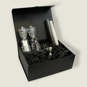 The London Acrylic Mill Christmas Gift Hamper by Cole & Mason includes a sleek black box with shredded paper, featuring a salt and pepper mill set, two spice tubes, and a metal funnel all neatly arranged inside.