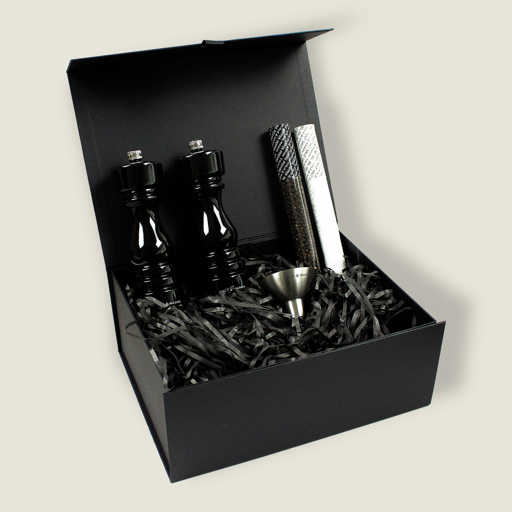 The London Black Gloss Mill Christmas Gift Hamper by Cole & Mason includes two black grinders, two sealed spice tubes, and a metal funnel, all presented in an open black gift box with black shredded paper.
