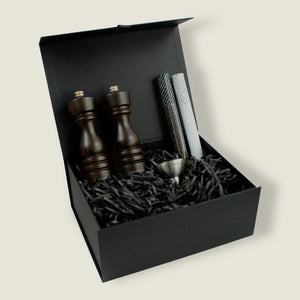 The Cole & Mason London Chocolate Wood Mill Christmas Gift Hamper features two wooden mills, pepper tube, metal funnel, and black shredded paper in a black gift box—an elegant choice for Christmas gift hampers.