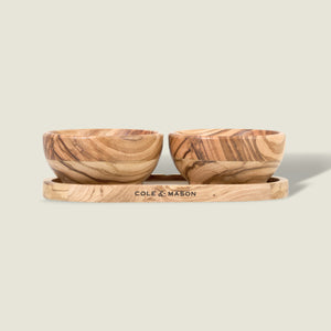 The Cole & Mason Portobello Olive Wood Pinch Pot Set features two small pots with unique grain patterns on a matching tray engraved with the brand name. The set is displayed against a plain, light beige background.