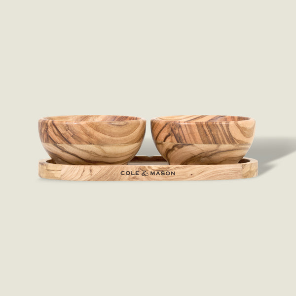 The Cole & Mason Portobello Olive Wood Pinch Pot Set features two small pots with unique grain patterns on a matching tray engraved with the brand name. The set is displayed against a plain, light beige background.