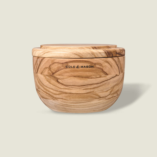 The Portobello Olive Wood Salt Cellar by Cole & Mason features natural grain patterns, a matching lid, and the brand logo on the front, adding timeless charm to your kitchen decor. Shown against a plain light background.