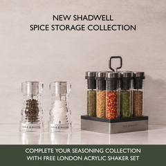 Shadwell Countertop Spice Storage featuring two clear acrylic spice grinders and a revolving spice rack containing eight airtight glass containers filled with various herbs and spices.