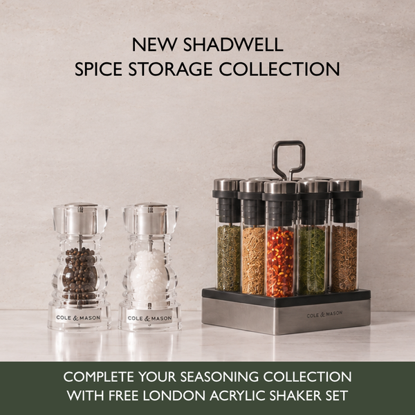 Shadwell Countertop Spice Storage featuring two clear acrylic spice grinders and a revolving spice rack containing eight airtight glass containers filled with various herbs and spices.