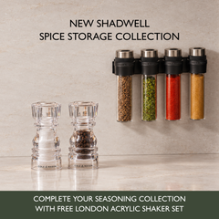 Four wall-mounted Shadwell Slim-Mount Spice Storage tubes positioned above two clear acrylic salt and pepper shakers, with text reading New Shadwell Spice Storage Collection and Complete your seasoning collection with free London acrylic shaker set.